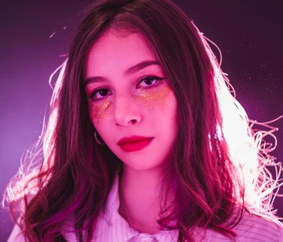 Vibrant portrait of a woman with glittery makeup, highlighted by a glowing backlight.