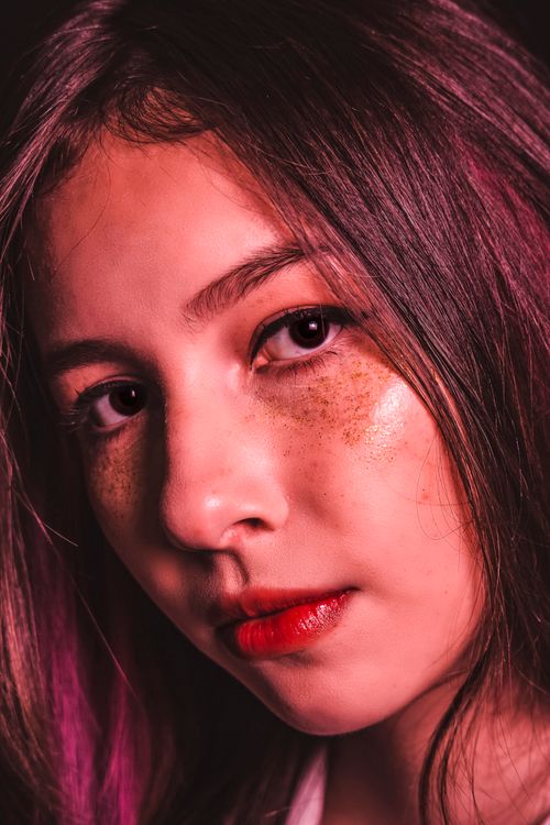 Free Intense close-up of a young woman with freckles and pink hair highlights in warm light. Stock Photo