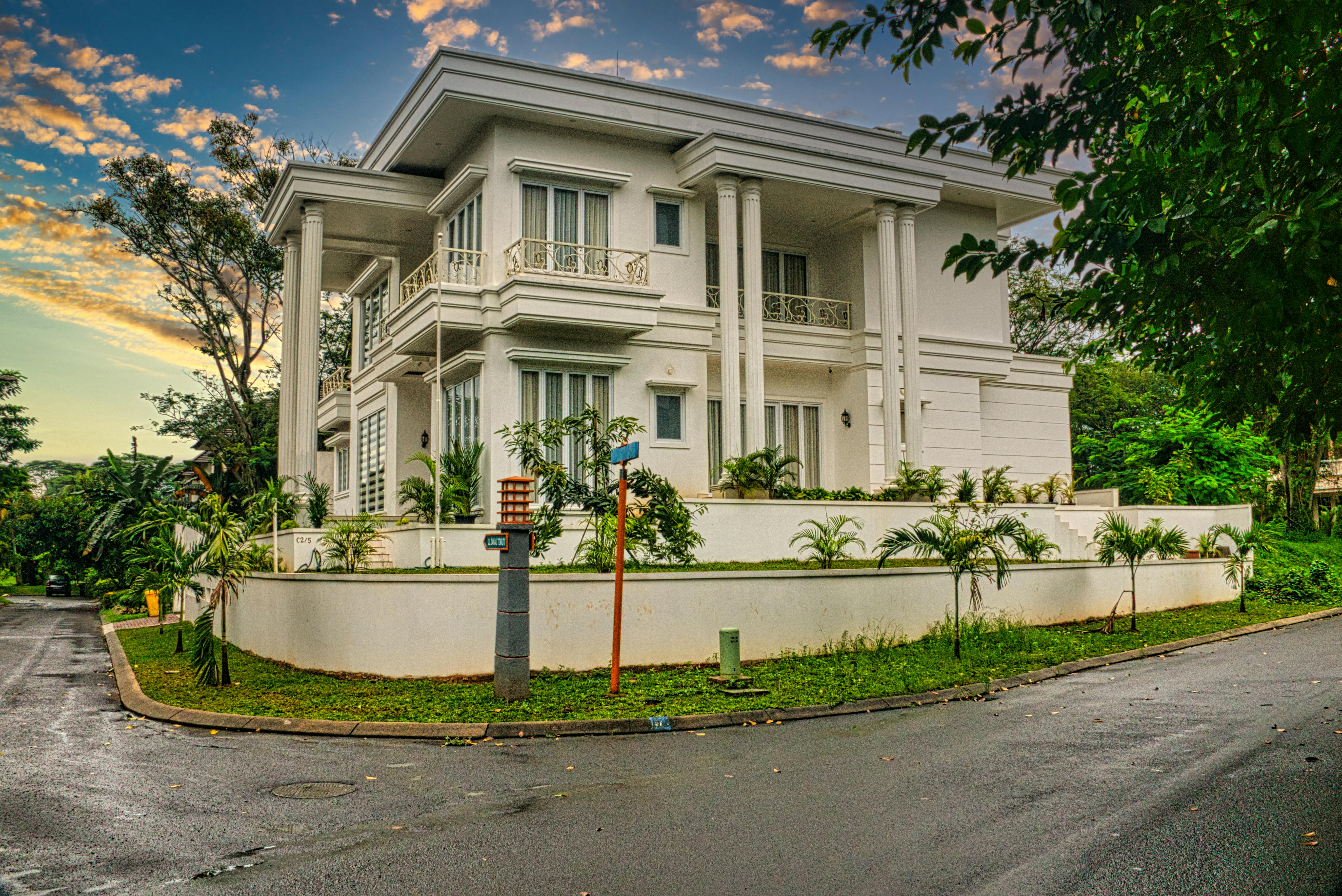 Free A modern two-story house with elegant columns and lush greenery on a corner lot in Banten, Indonesia. Stock Photo