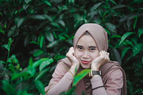 Free Charming portrait of a young woman in a pink hijab smiling amidst lush greenery. Stock Photo