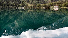 宁静的山间湖泊旁有一所房子，四周树木郁郁葱葱，倒映在平静的水面上