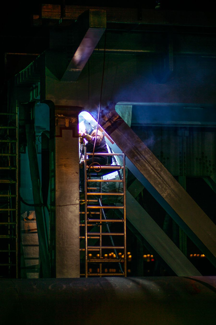 Welder working high on the finished structural steel frame at dusk