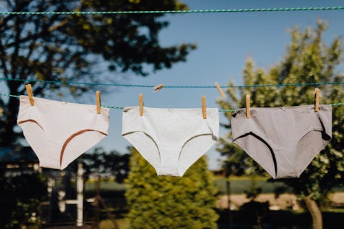 From below of washed feminine underwear hanging on rope with clothespins outdoors on sunny summer weather against blue sky and green trees