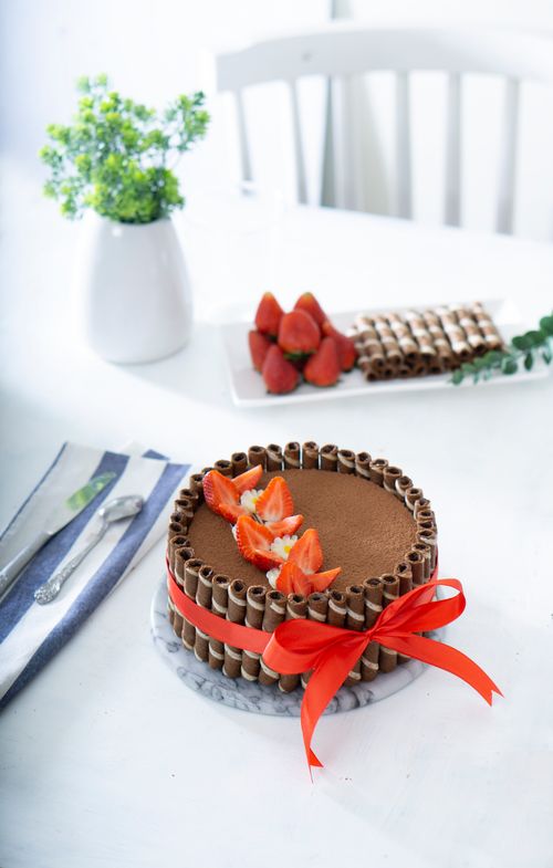 Free Elegant chocolate cake adorned with strawberries and a red ribbon on a white table. Stock Photo