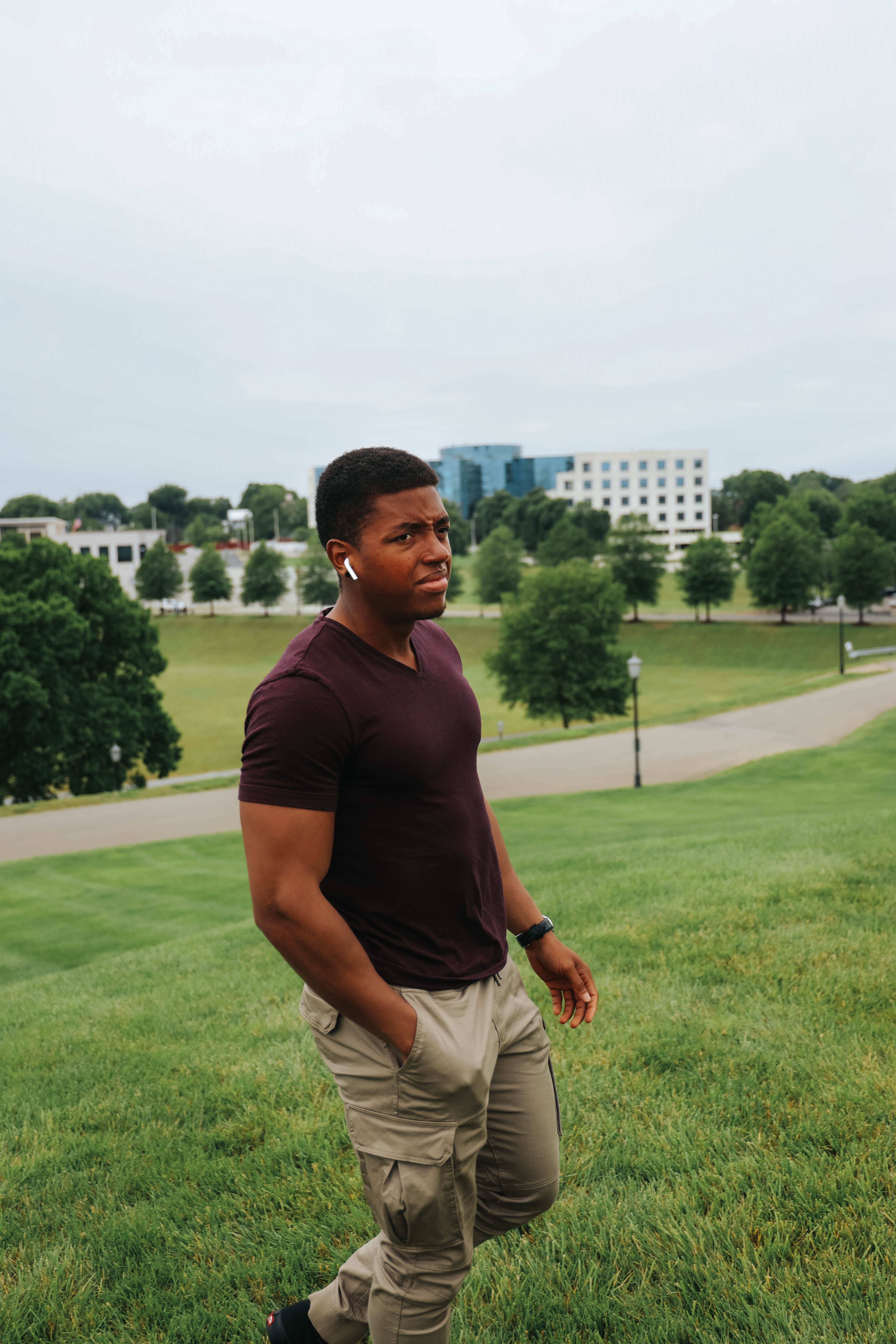 Full body side view of young sporty African American male in casual clothing looking away and listening music while walking in park with hand in pocket