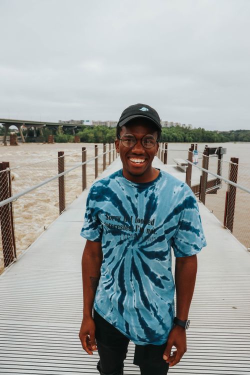 Free Positive happy black male with toothy smile in t shirt with eyeglasses and cap spending free time on pier near river Stock Photo