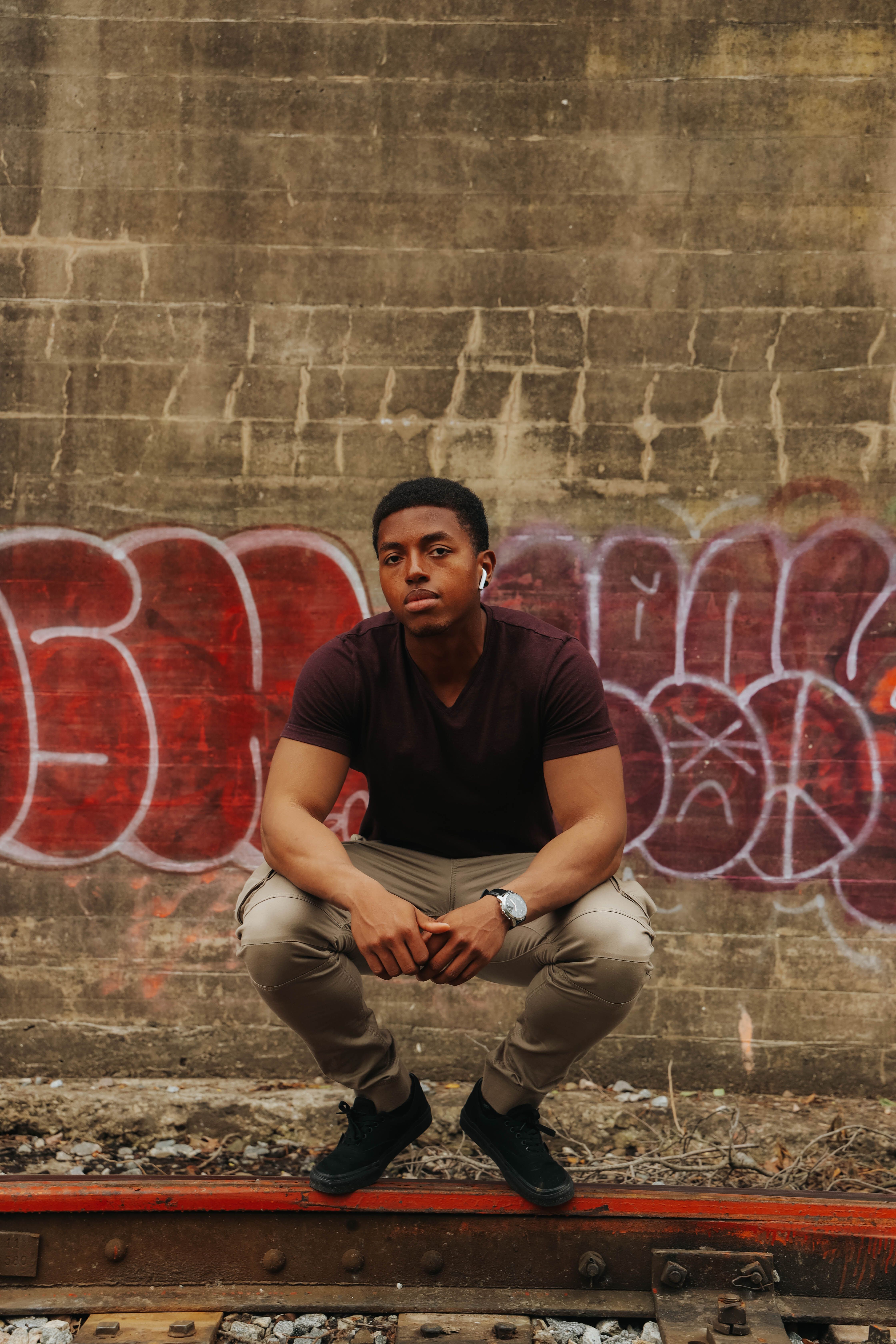 Street style portrait of a man squatting on railway tracks against graffiti wall.