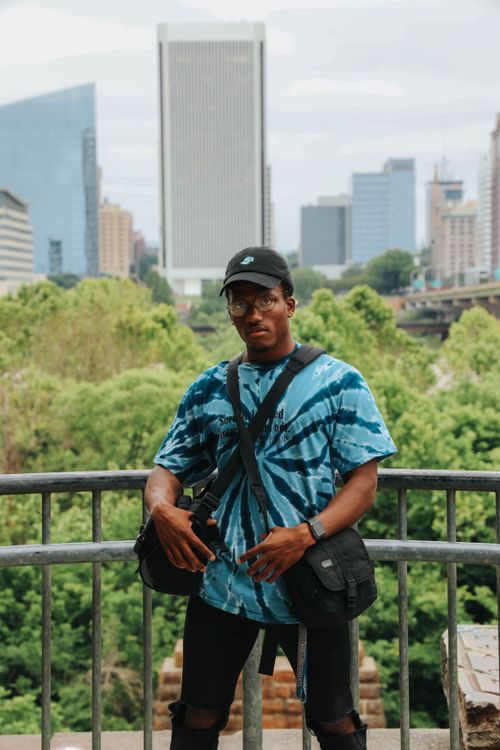Free Ethnic male in bright t shirt with bags on shoulders and eyeglasses spending cloudy day on urban area viewpoint in modern city Stock Photo
