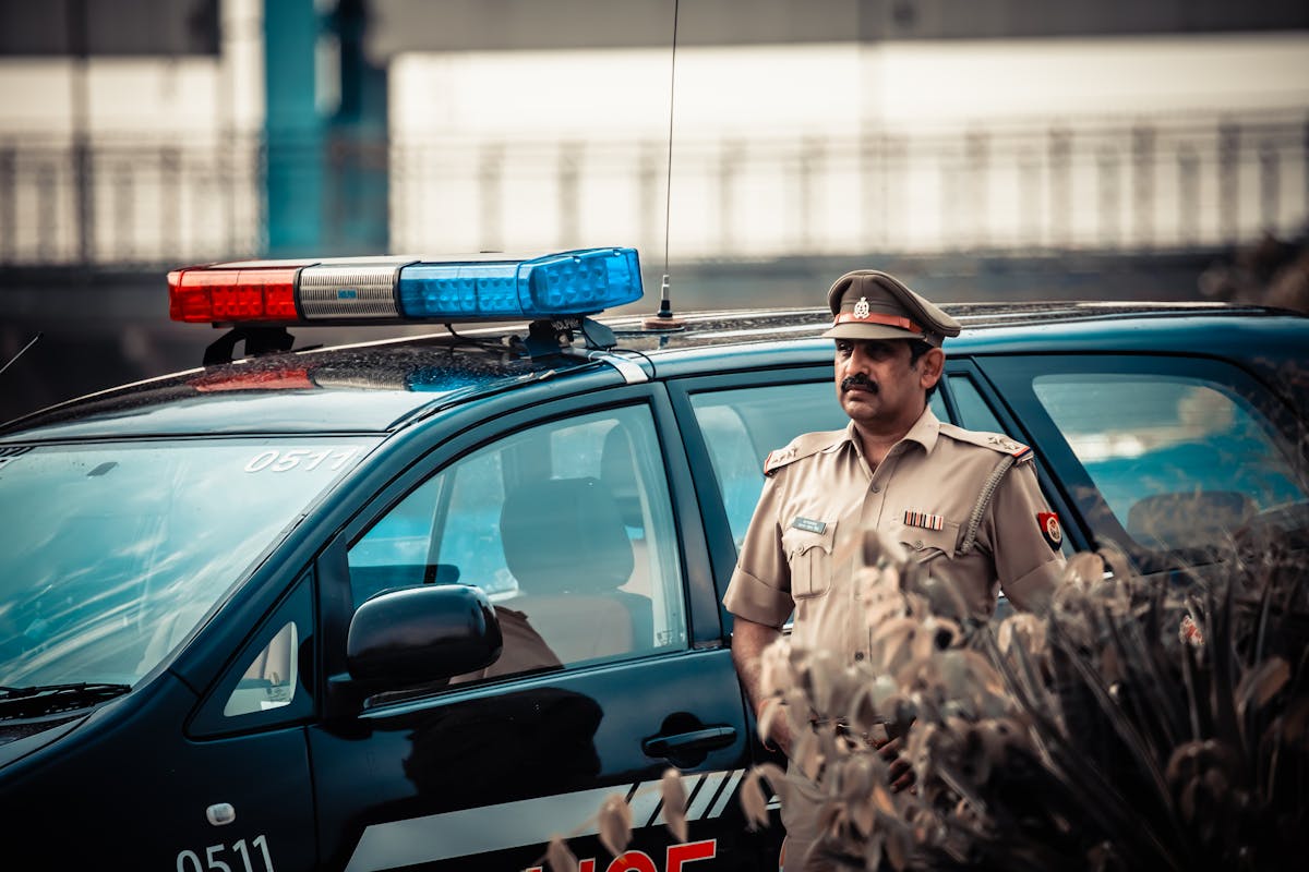Male in uniform standing near patrol car with flashing lights and looking away