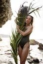 一位身穿泳装的年轻女子在热带海滩上拥抱棕榈叶，散发出夏日的气息
