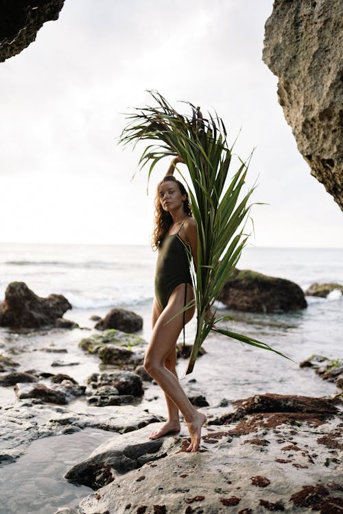 Young model in swimming suit with palm leaf at seaside