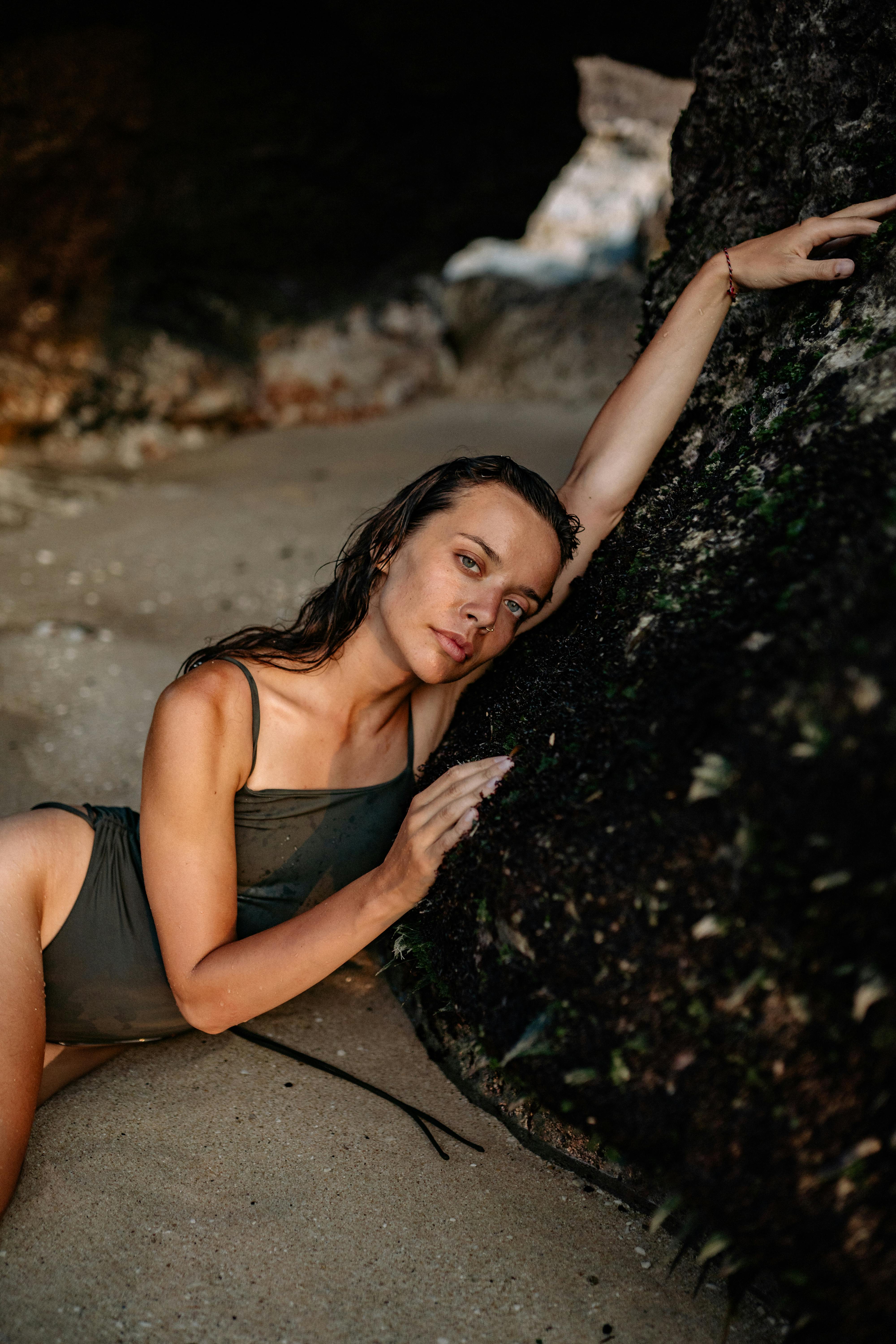 Graceful female model near rough rock on sandy beach · Free Stock Photo