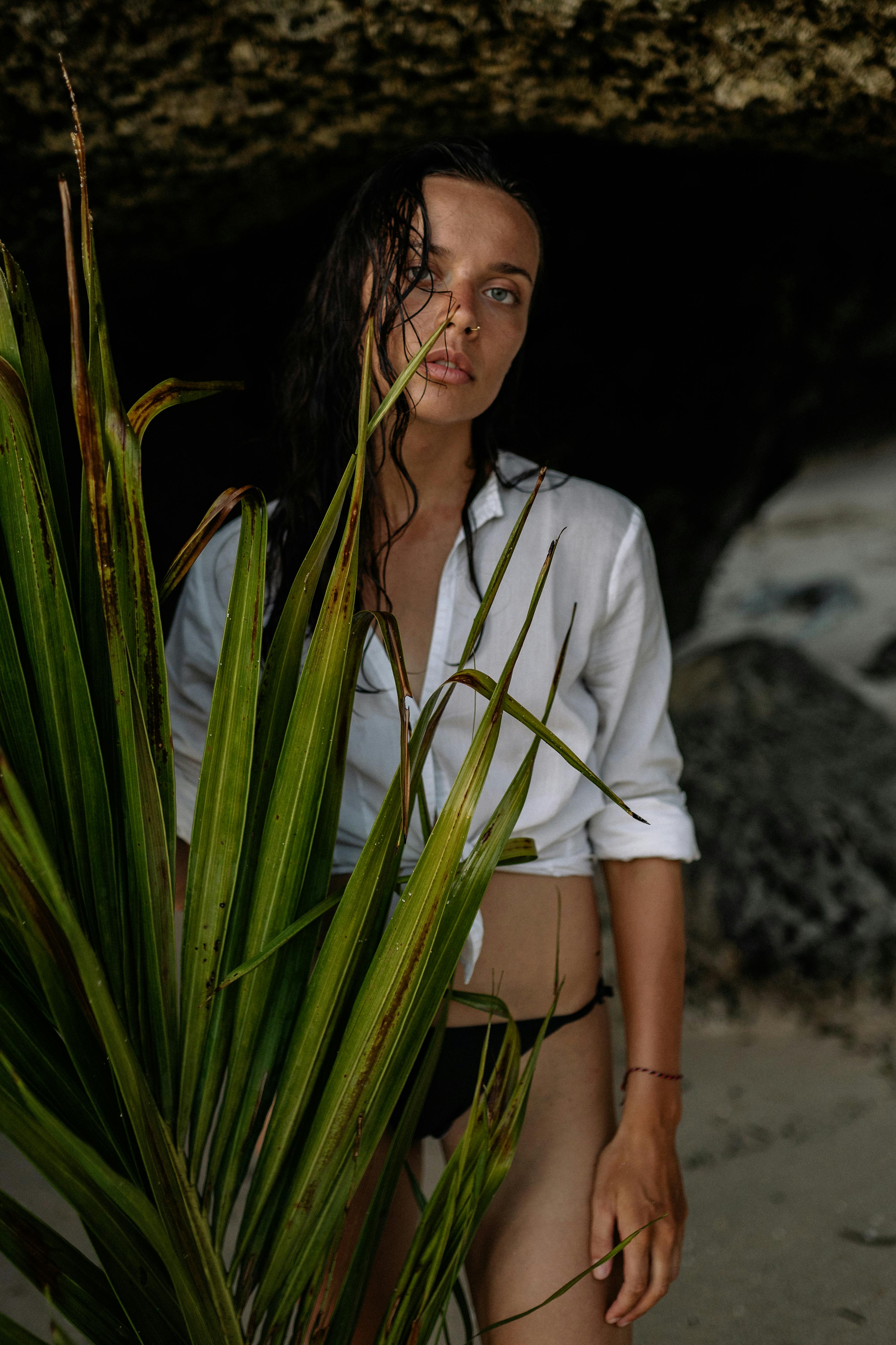 calm woman in bikini holding branch of palm in cave