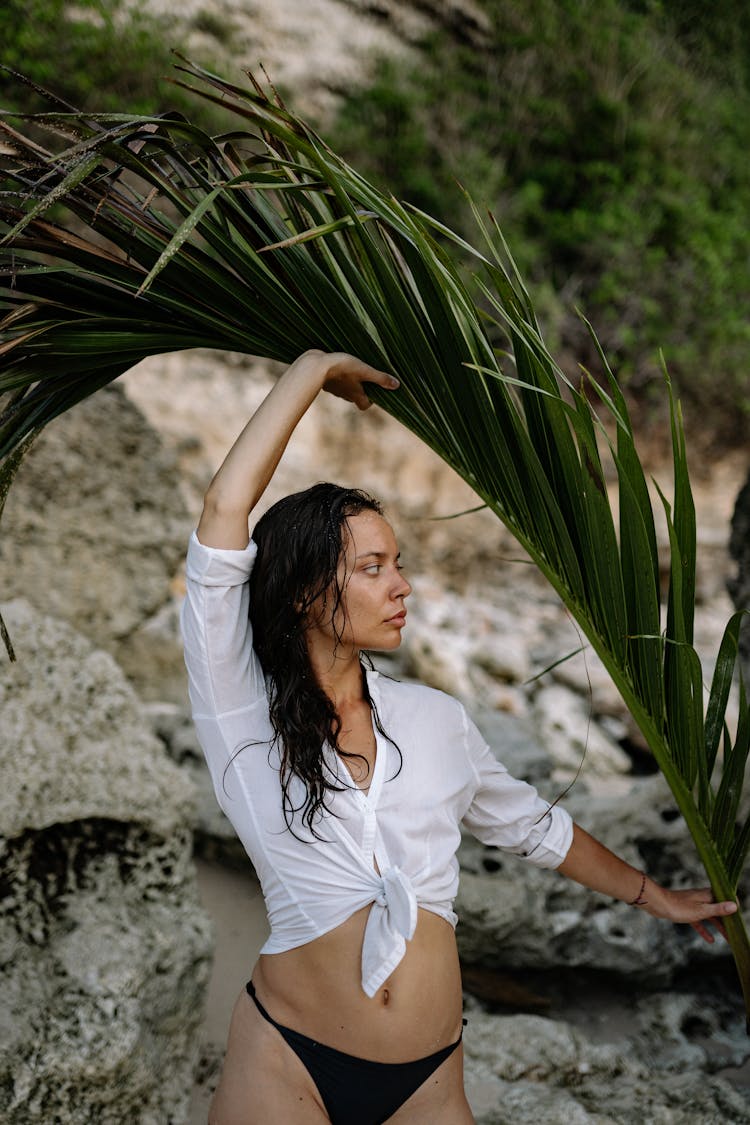 Slim Woman In Bikini And Shirt Holding Palm Branch On Shore