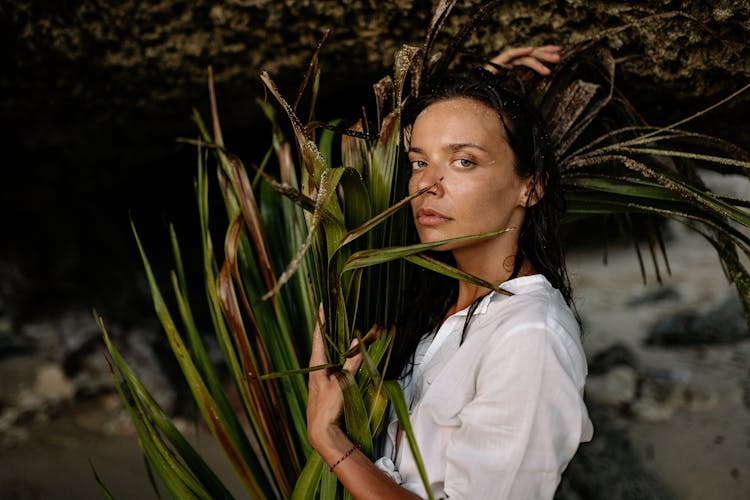 Serious Woman Cuddling Calamus Leaves Against Cave