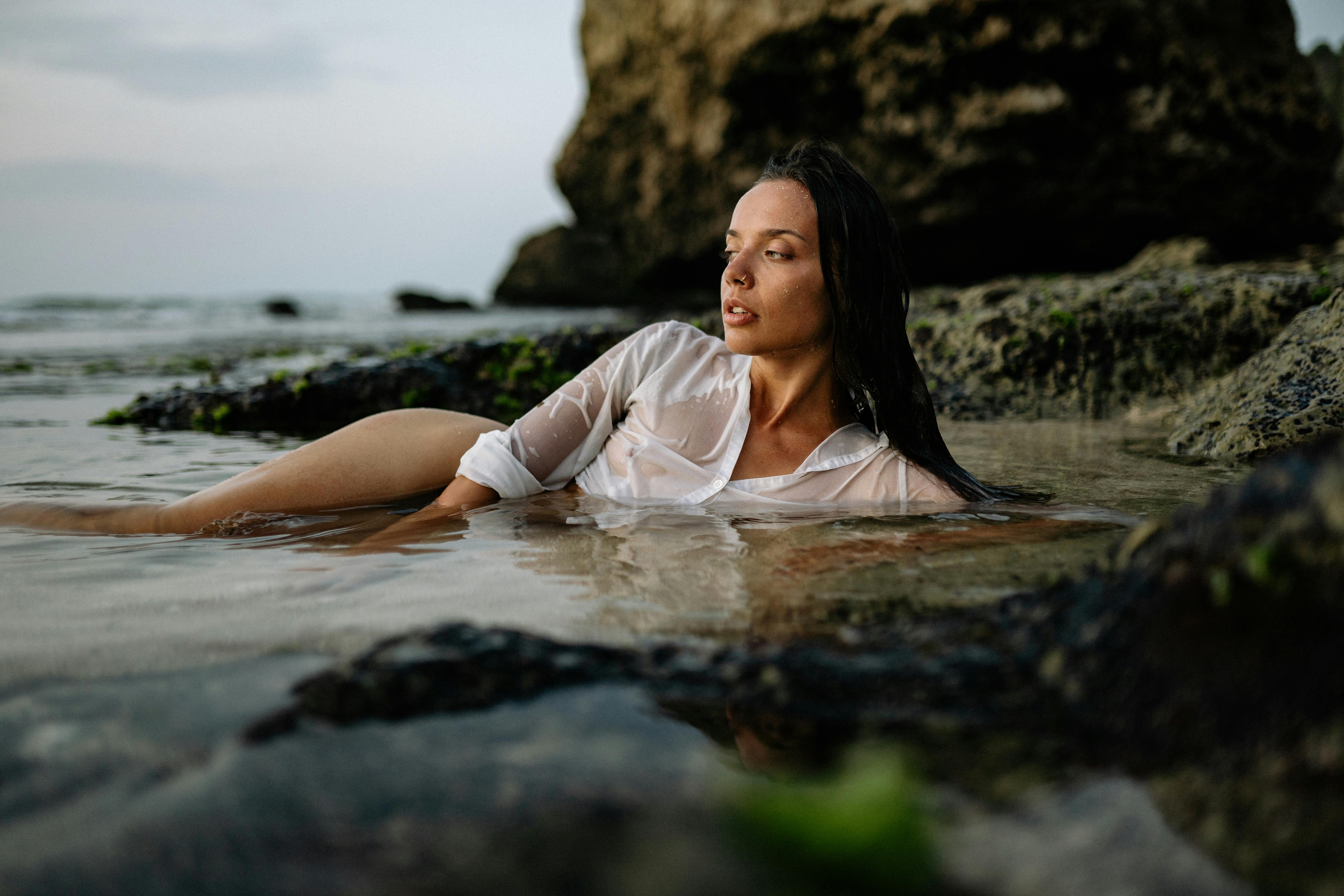 graceful woman resting on rocky seashore in wet shirt