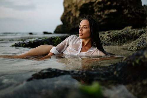 Graceful woman resting on rocky seashore in wet shirt