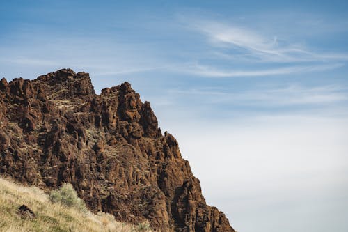 Low angle of rough mount with pointed peaks near golden grass under blue cloudy sky