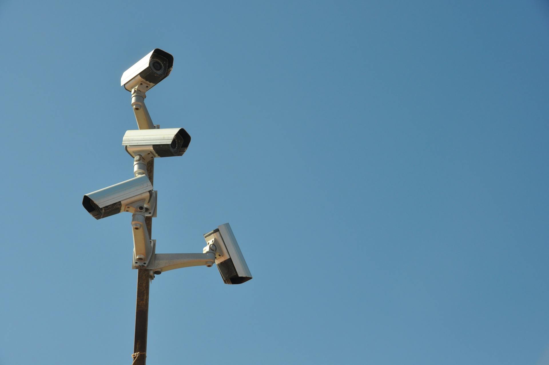 Four surveillance cameras mounted on a metal post under a clear blue sky, highlighting security technology.