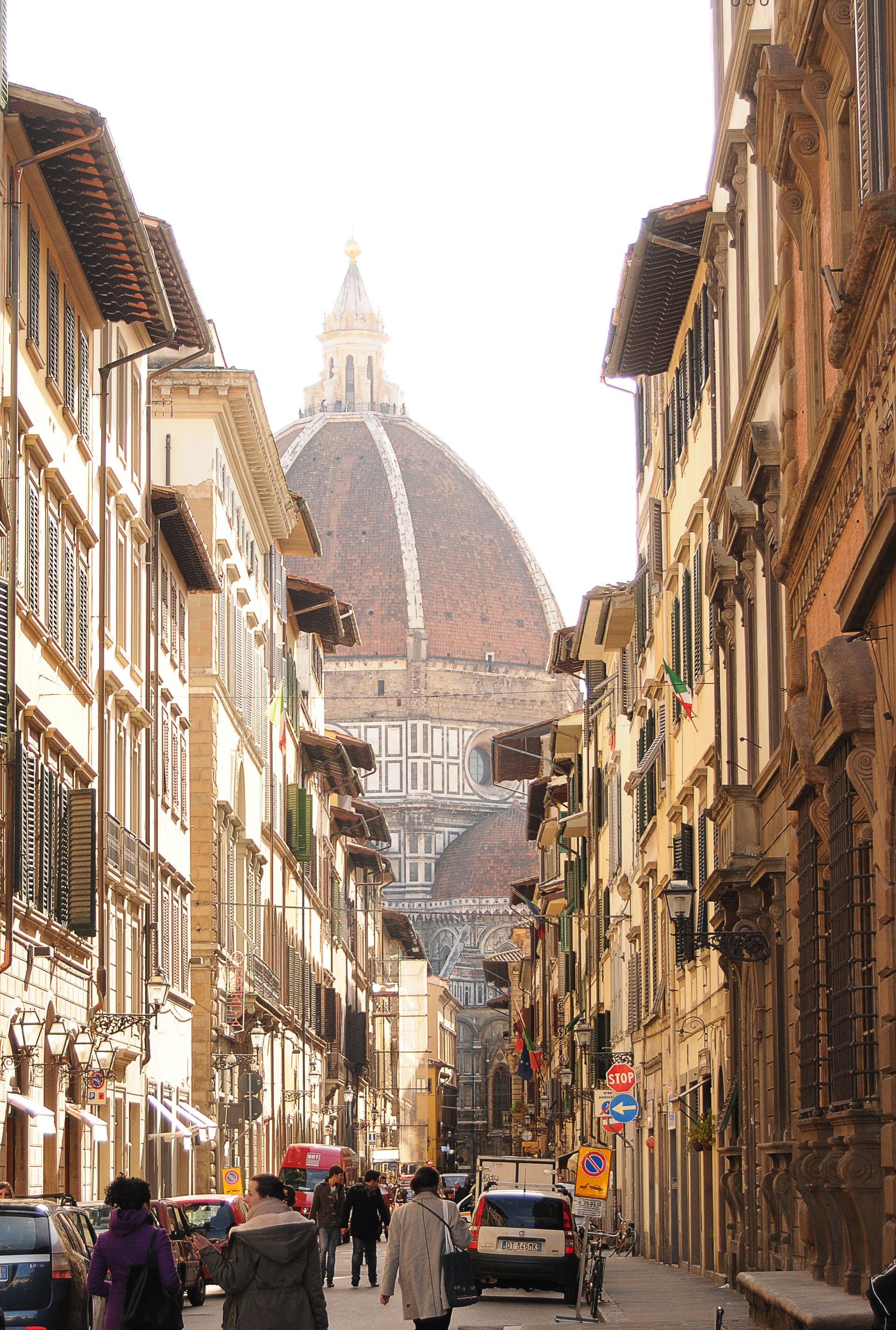 People walking down a narrow street toward the dome of Florence Cathedral in Italy