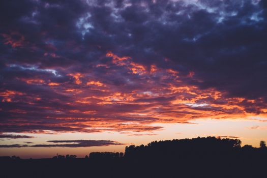 Vibrant sunset over a silhouetted landscape with dramatic cloud formations.