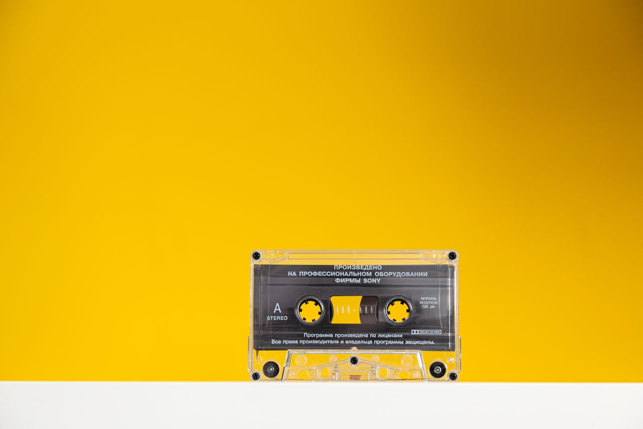 a retro cassette tape with clear casing on a bold yellow background ev