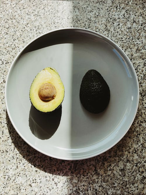 Top view of halves of fresh avocado placed on gray plate with half in shadow