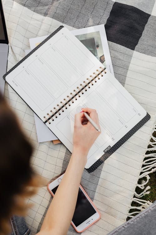 Student writing in organizer while sitting on picnic rug