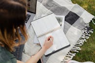 Crop woman taking notes in notebook while sitting in park