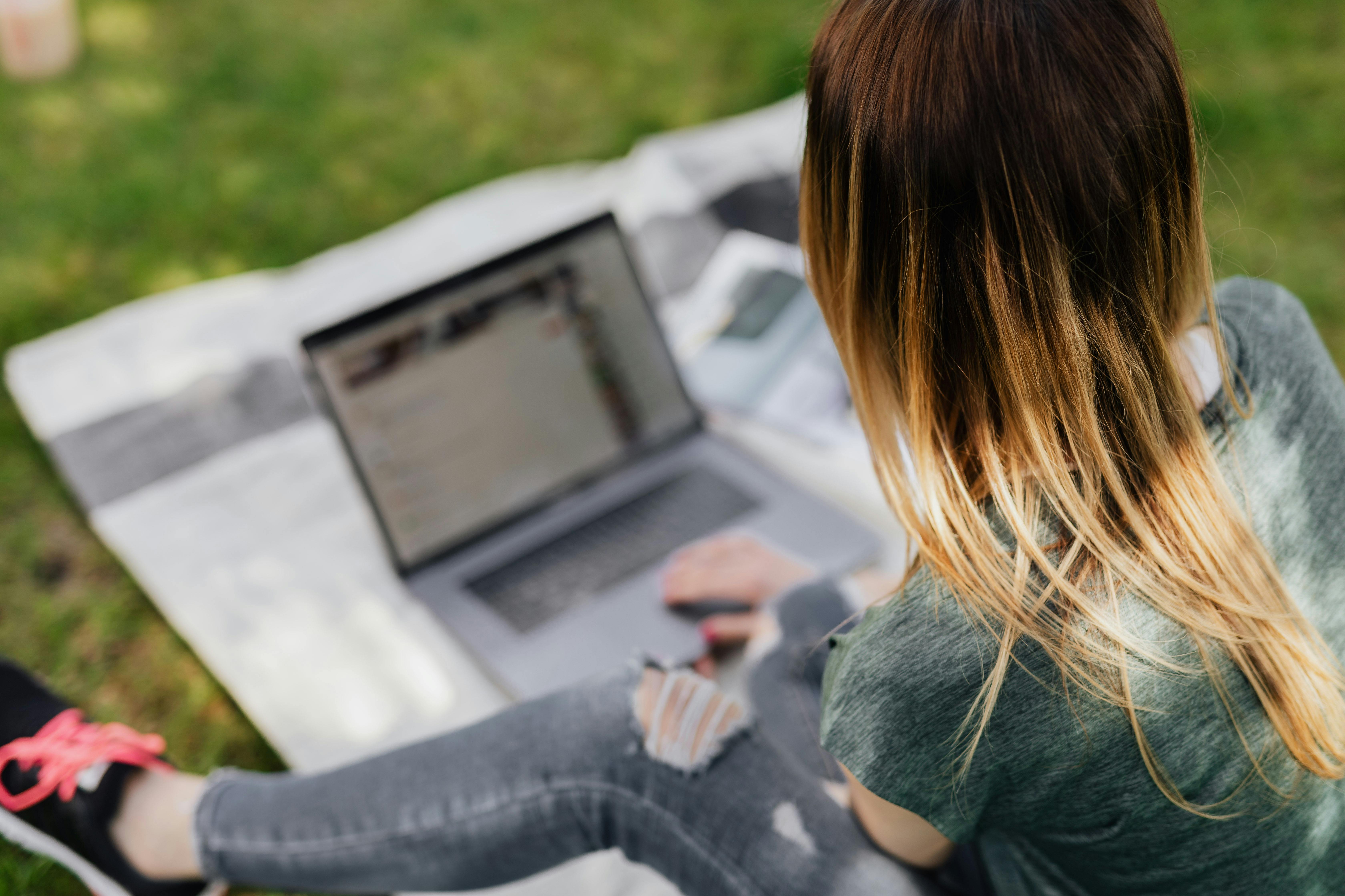 youngster surfing net on laptop while relaxing in park