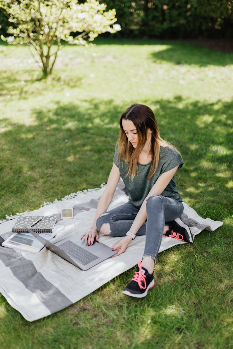 Female Student Working On Laptop While Doing Homework In Park