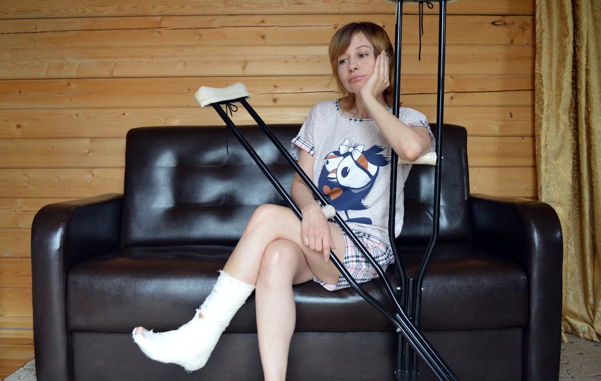 Free Unhappy woman with trauma in leg sitting on sofa and leaning on crutches Stock Photo