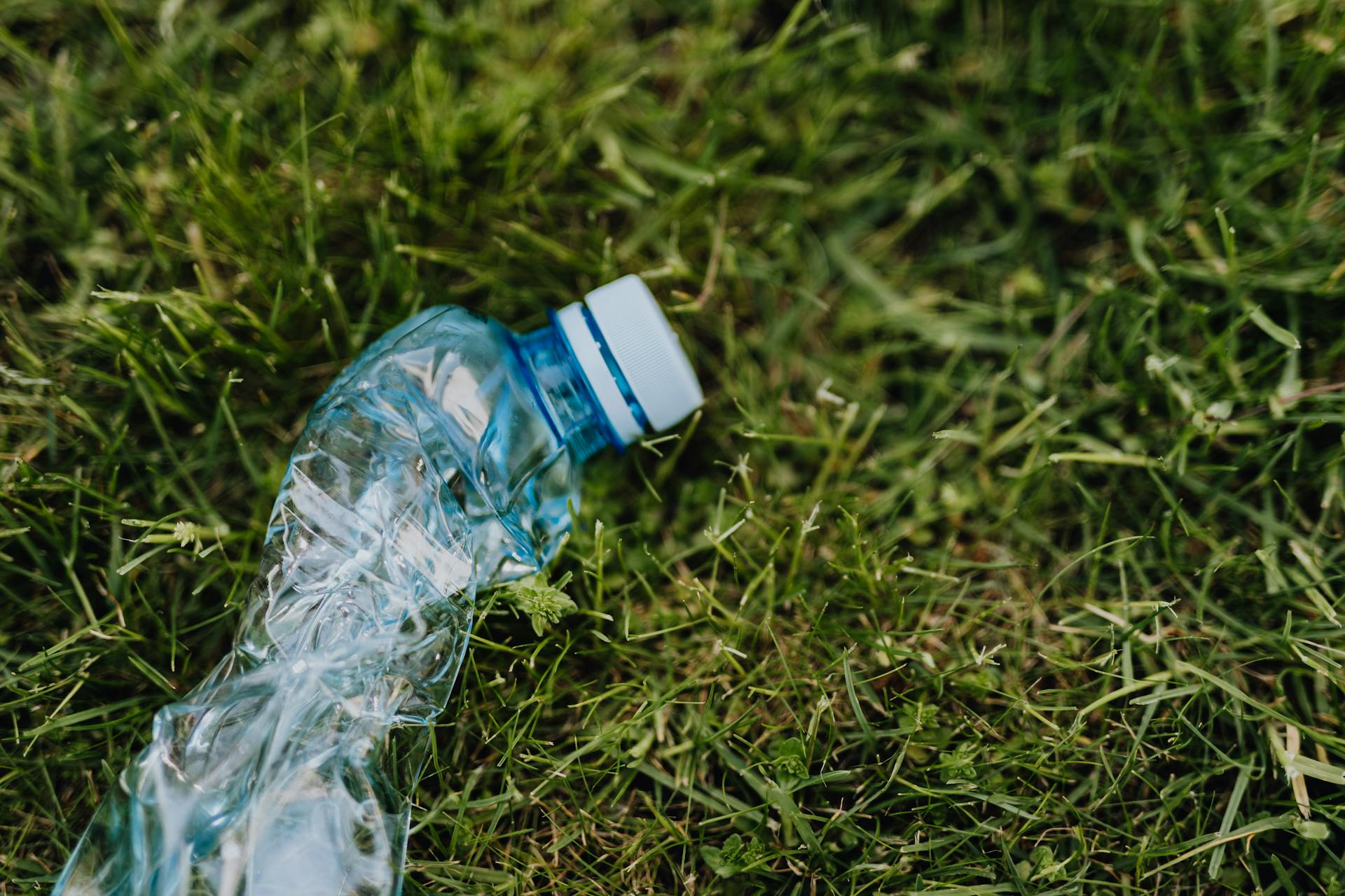 From above of blue crumpled plastic bottle thrown on green park lawn on sunny summer day