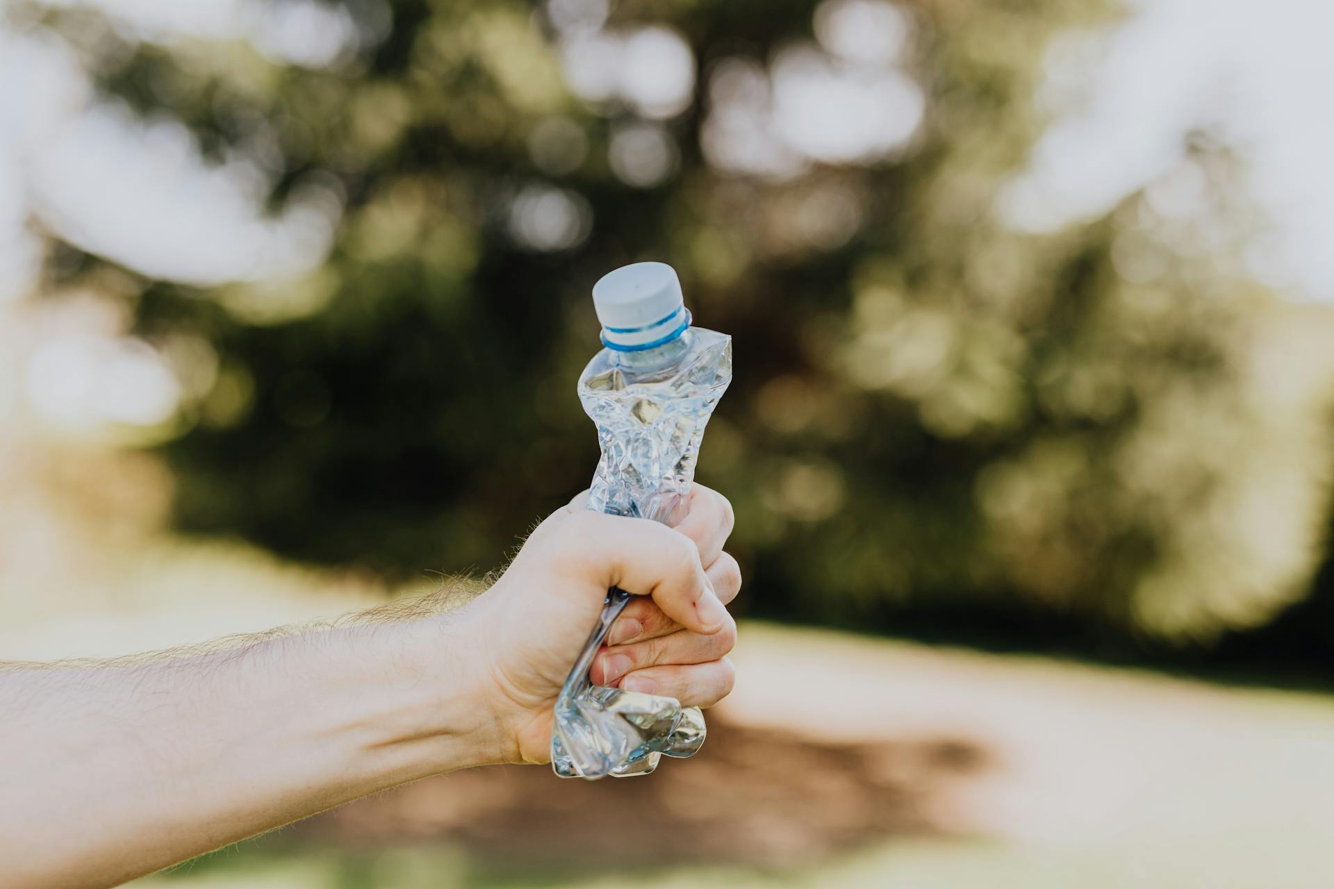 Crop man crushing plastic bottle