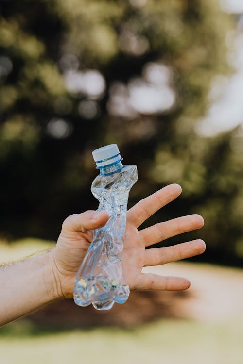 Free Crop anonymous person demonstrating squished used plastic bottle on sunny summer day in park Stock Photo