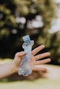 Crop anonymous person demonstrating squished used plastic bottle on sunny summer day in park