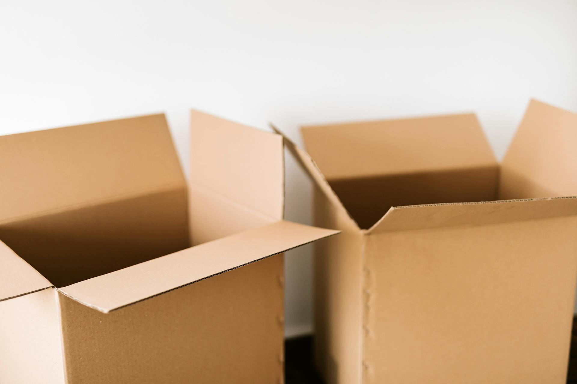 Opened carton boxes placed on dark surface against white plain wall in daylight before moving out