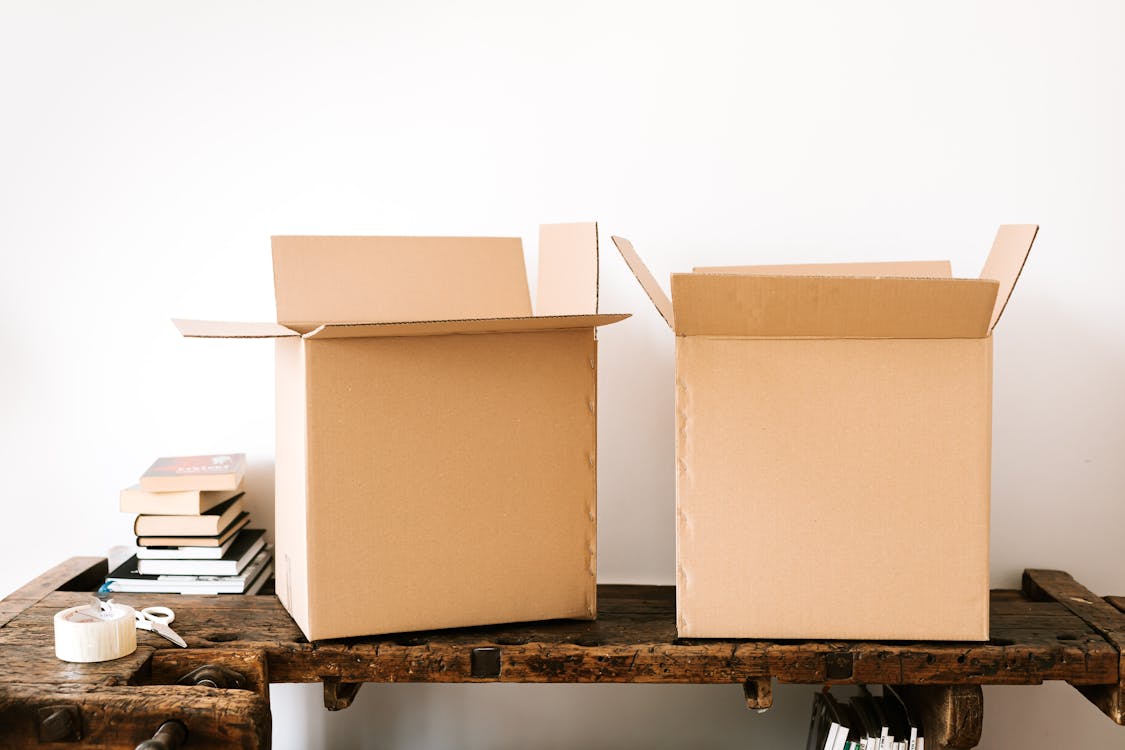 Free Opened carton boxes and stacked books placed on shabby wooden desk with tape against white wall Stock Photo