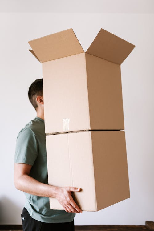 Free Side view anonymous male in casual clothes carrying stack of opened carton boxes while moving into new apartment Stock Photo