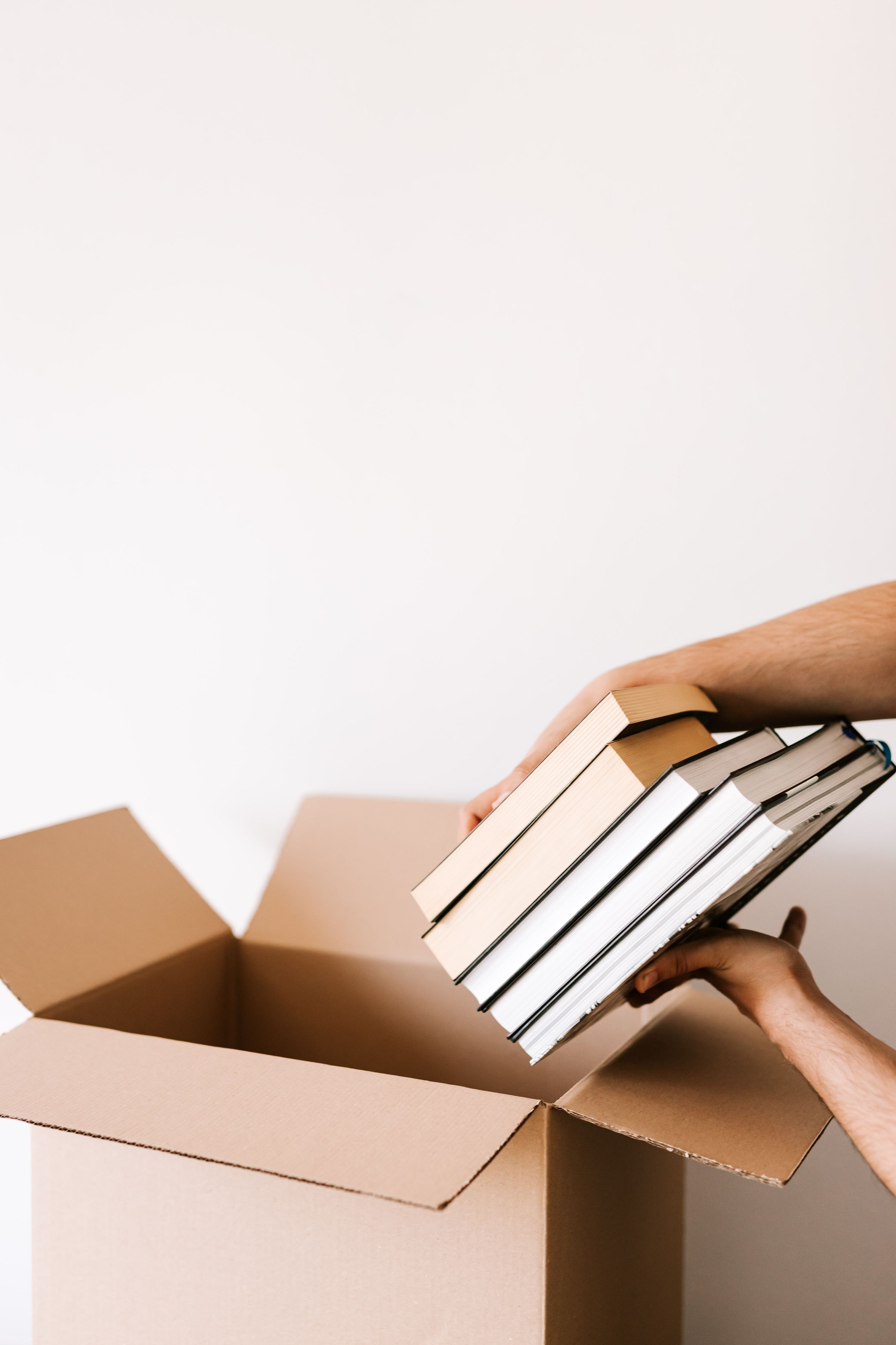Hands packing a stack of books into a cardboard box