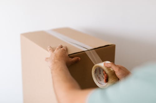 Crop man sealing carton box with tape