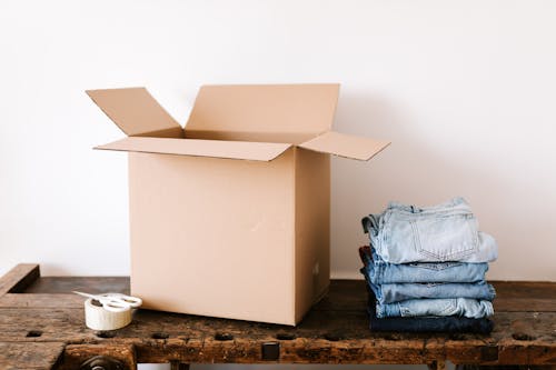 Stack of jeans near carton box and tape