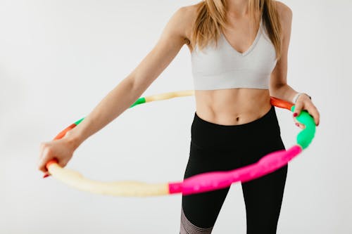 Free Crop faceless fit lady in black leggings and sports bra practicing fitness exercises with hula hoop against gray background Stock Photo