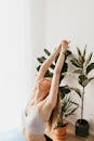 From above sporty calm female in gray sports bra performing Upward Salute exercise while practicing yoga in light living room