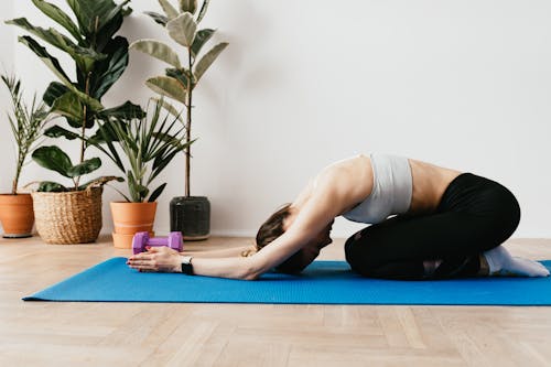 Side view full length anonymous sporty lady in activewear stretching in Child Pose on yoga mat during post workout stretch at home