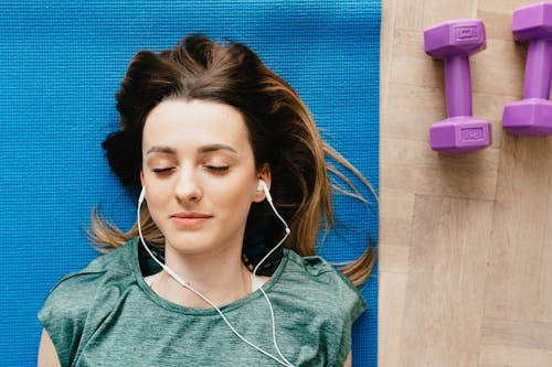 Free Woman listening to music in earphones while resting after home workout Stock Photo