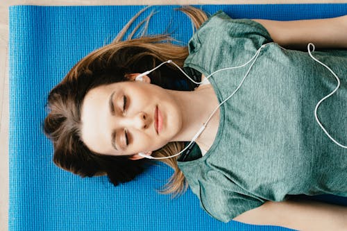 Free Tranquil woman resting on yoga mat in earphones at home Stock Photo