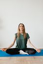 Calm slim female in sports clothes sitting with crossed legs in Padmasana pose on yoga mat while meditating with closed eyes in flat