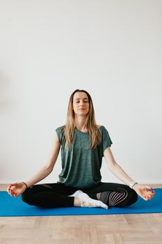 Calm slim female in sports clothes sitting with crossed legs in Padmasana pose on yoga mat while meditating with closed eyes in flat