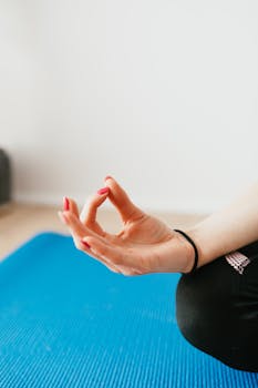 A woman's hand in a yoga mudra pose on a blue mat, promoting calmness and mindfulness.